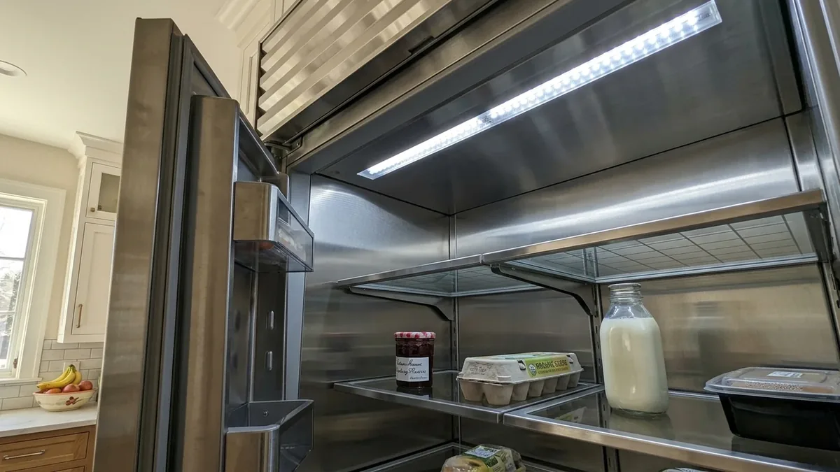 Interior LED light strip glowing inside an open stainless Sub-Zero refrigerator in daylight