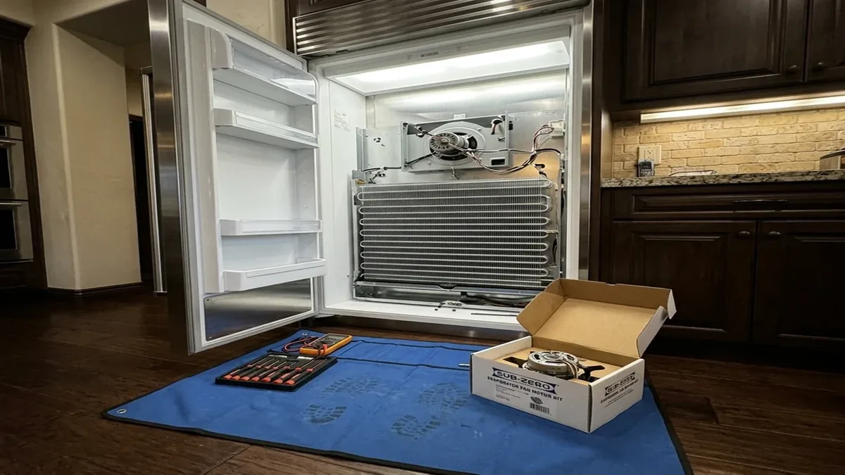 Replacement fan motor in its box beside an open Sub-Zero refrigerator on a service mat